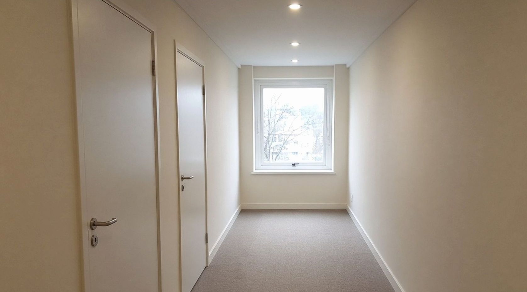 Couloir d’étage, portes blanches sans numéro, fenêtre au fond